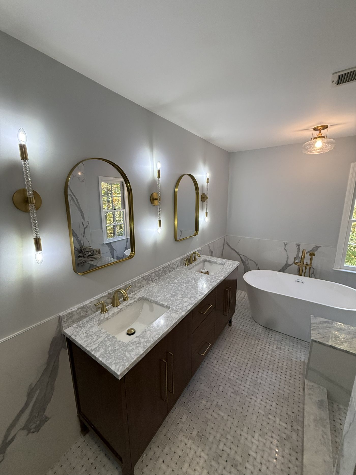 Brass sconces between arched mirrors over a double vanity, with a freestanding tub