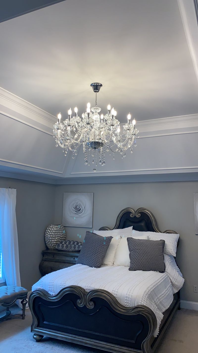 Crystal chandelier centered under a tray ceiling above a bed