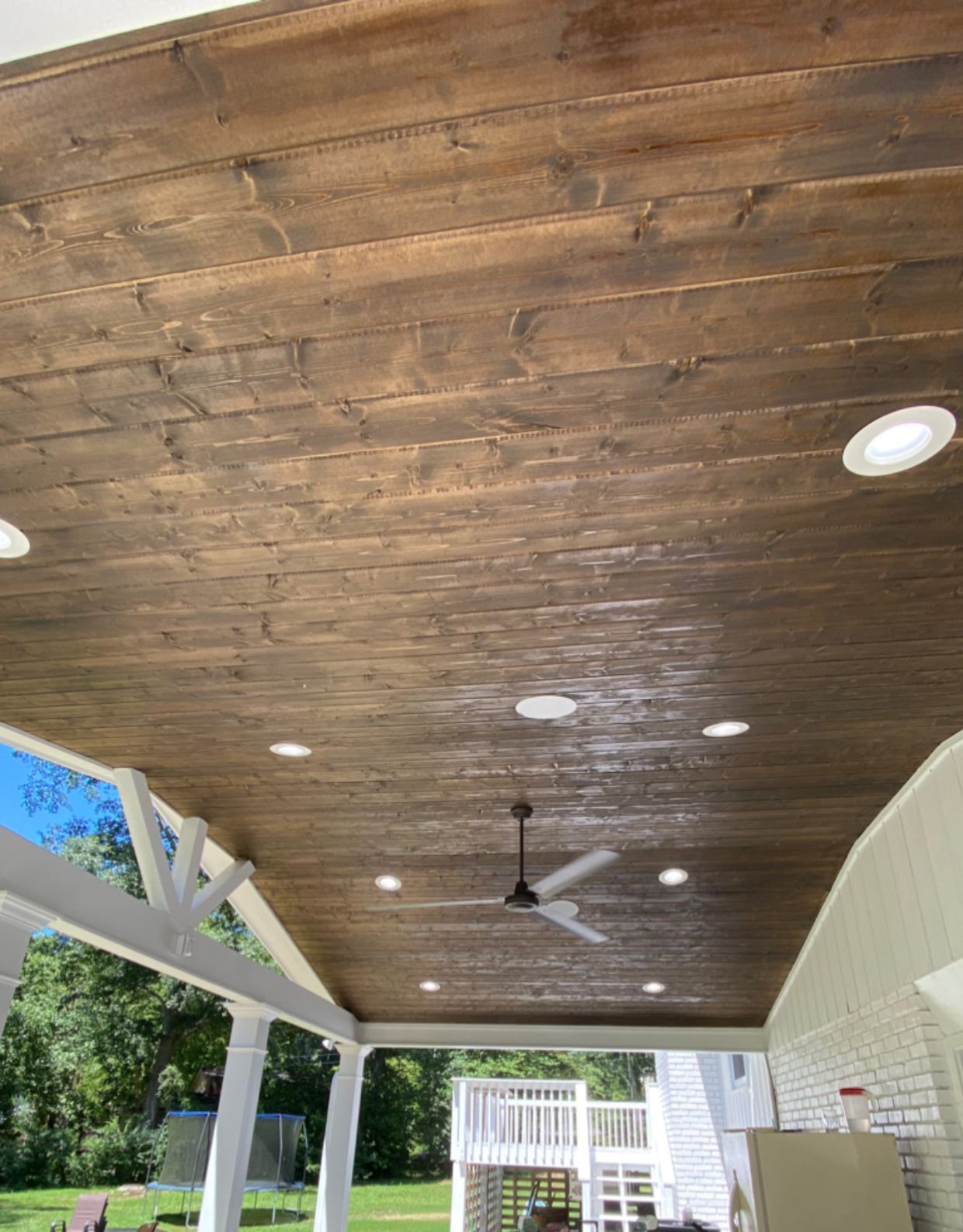 Recessed lights and a ceiling fan in a stained wood porch ceiling