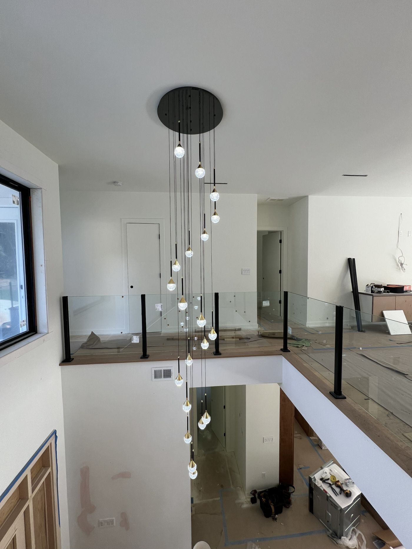 Tall cascade of crystal drop pendants in a two-story stairwell with a glass railing